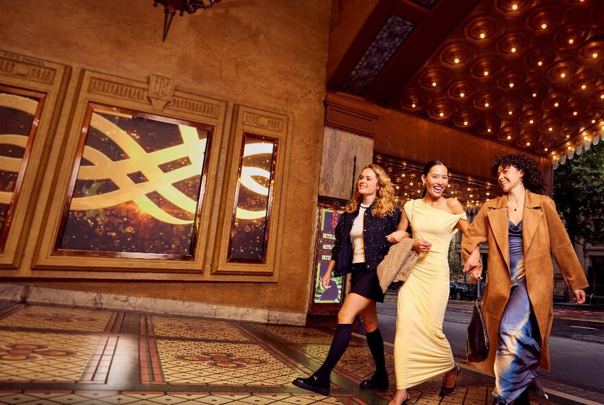 Three people striding into the Regent Theatre tiled entry with lights and city street in the background.