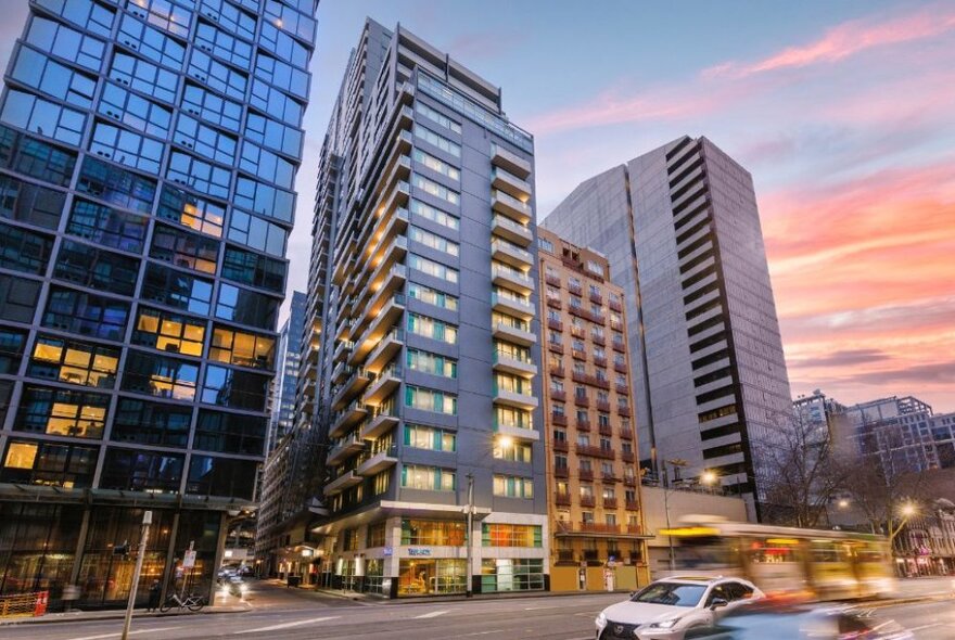 Hotel exterior at dusk next to neighbouring high-rise buildings.