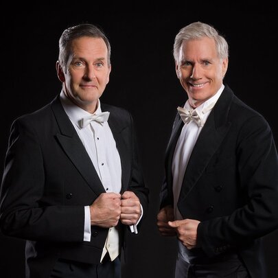 Comedian Colin Lane and opera singer David Hobson, both wearing black tuxedos with tails and white bowties.