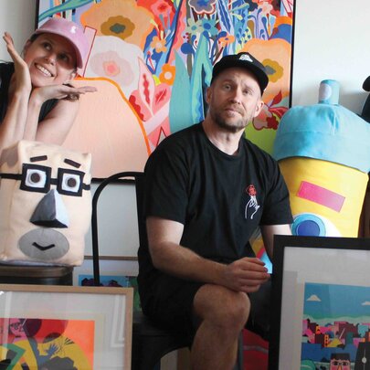 Artists Ed Bechervaise (Unwell Bunny) and Lucie Kershaw in a gallery setting surrounded by colourful, playful sculptures and paintings. 