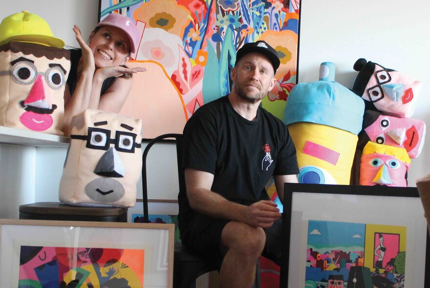 Artists Ed Bechervaise (Unwell Bunny) and Lucie Kershaw in a gallery setting surrounded by colourful, playful sculptures and paintings. 