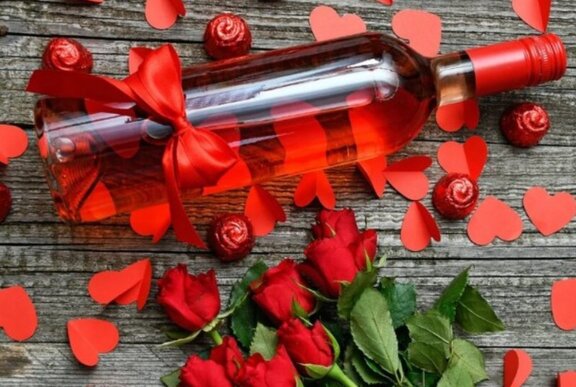 A cleanskin bottle of rose wine lying on a rustic wooden table with red paper hearts and long-stem roses.