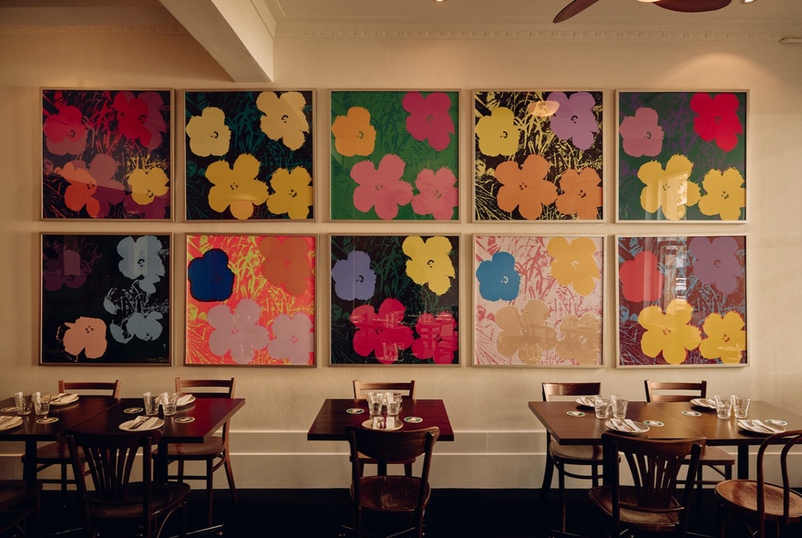 An empty restaurant dining room with 10 matching pictures of flowers on the wall. 
