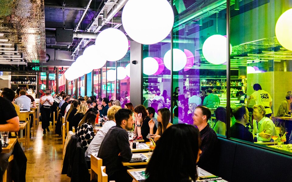 People dining in a modern restaurant with rainbow lighting and big orb lights above.