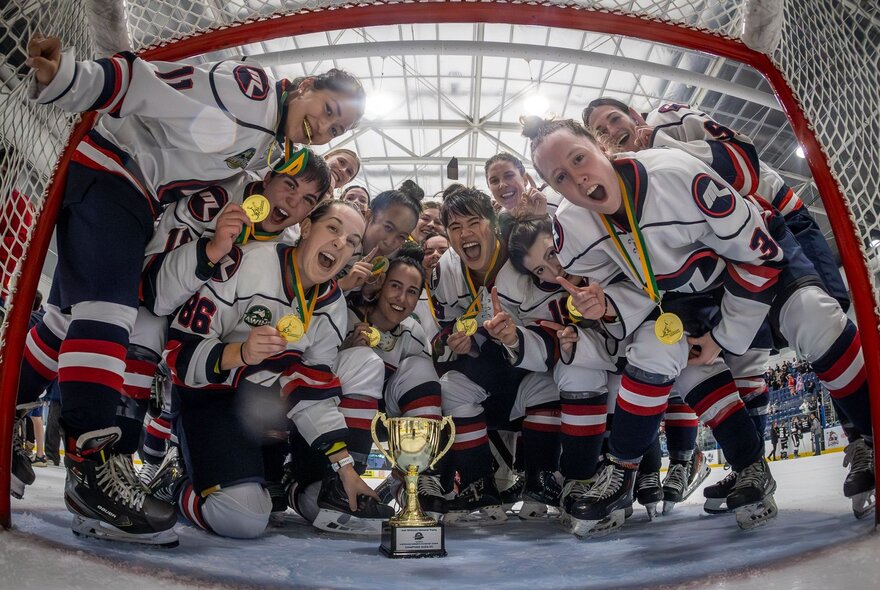 A fish-eye photo of the women's ice hockey champion team posing with the trophy after a win. 