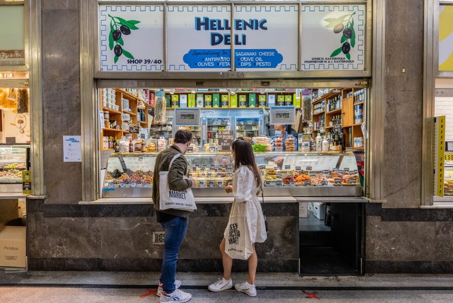 A couple shopping at a Greek deli inside a market.