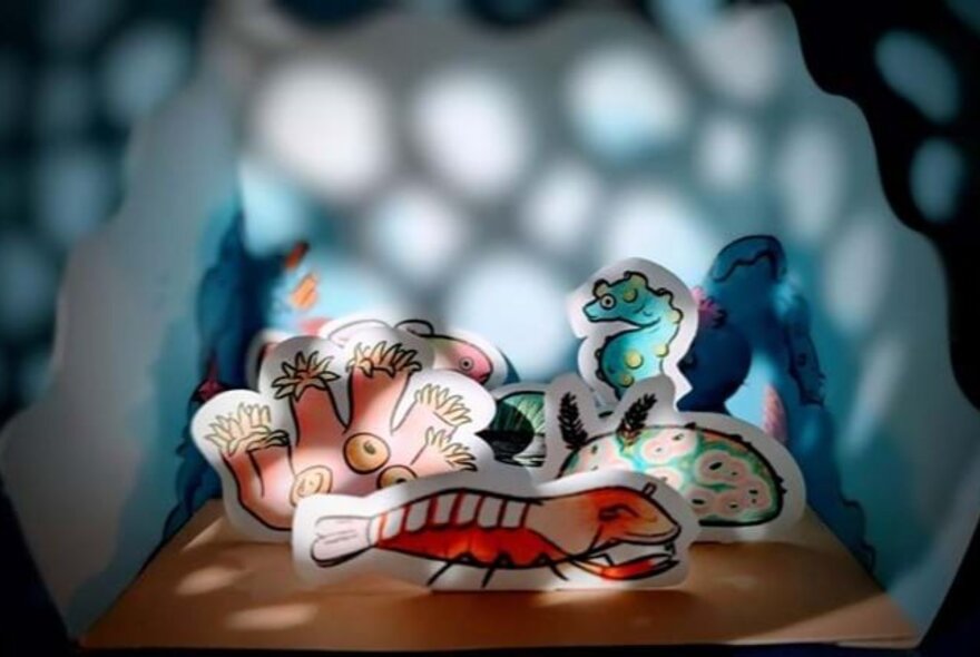 Paper cutouts of cartoonish creatures in a diorama with dappled light cast over it.