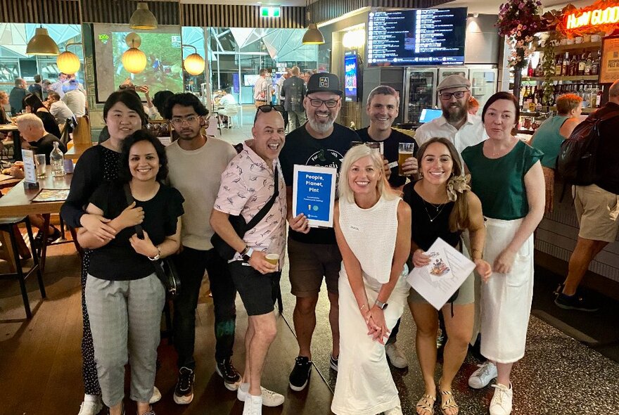 A group of people standing together in a pub, some holding certificates, all smiling at the viewer.