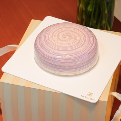 A purple coloured cake sitting on top of a yellow striped box.
