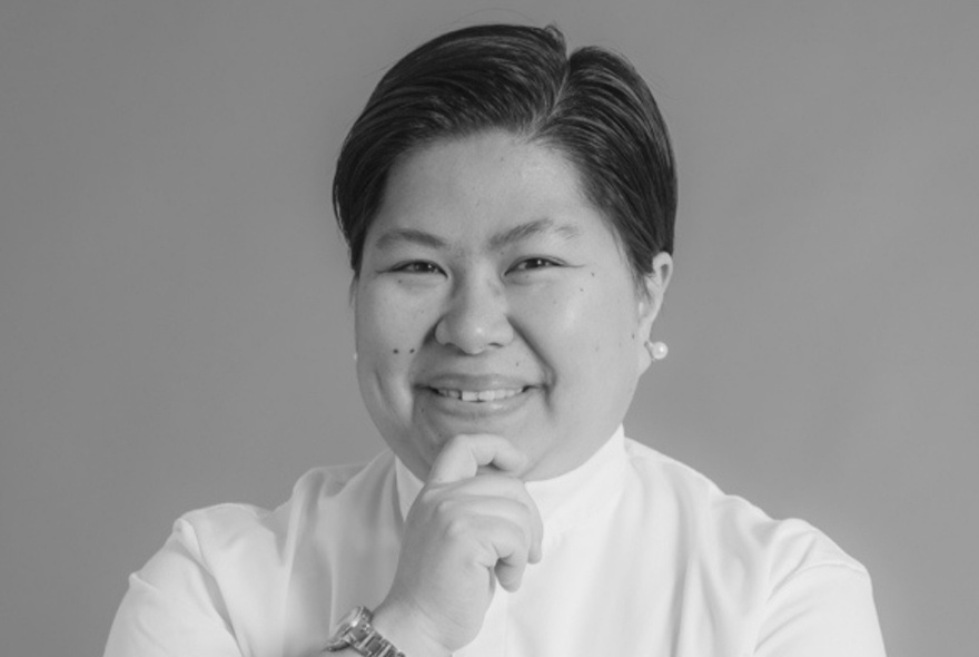 Black and white portrait of a female chef with short black hair wearing a white chef's shirt, posing with her forefinger on her chin.
