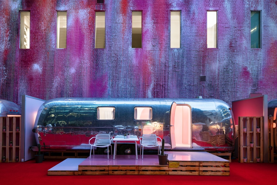 Vintage 1970s silver airstream trailer set against a building backdrop with a small deck out the front with two chairs.