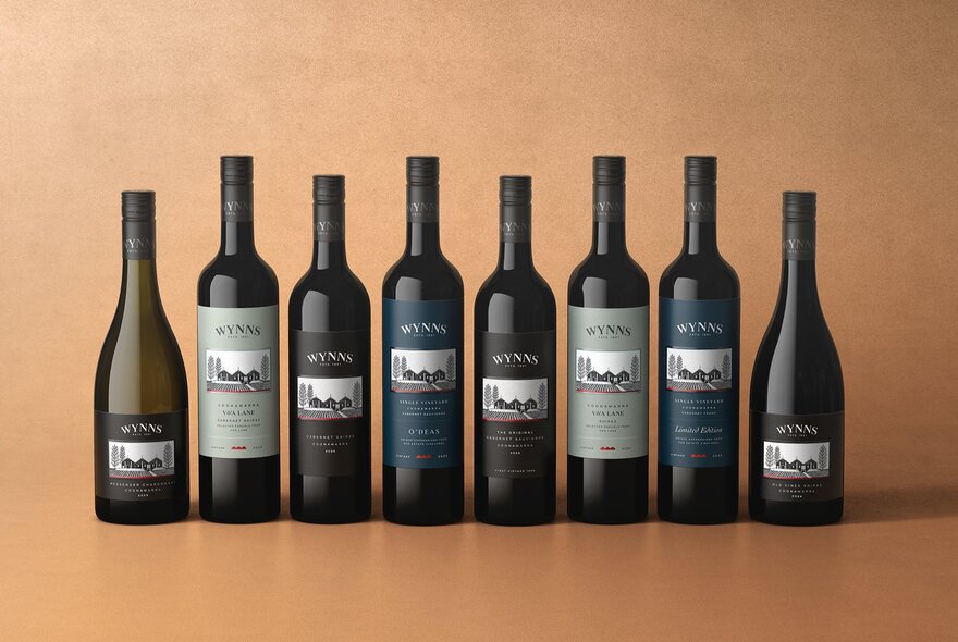 Eight bottles of Coonawarra wine lined up in a row against an orange background.