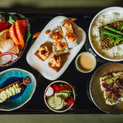 A Japanese bento tray with a selection of gourmet tasters including nori rolls, yakitori and scallops.