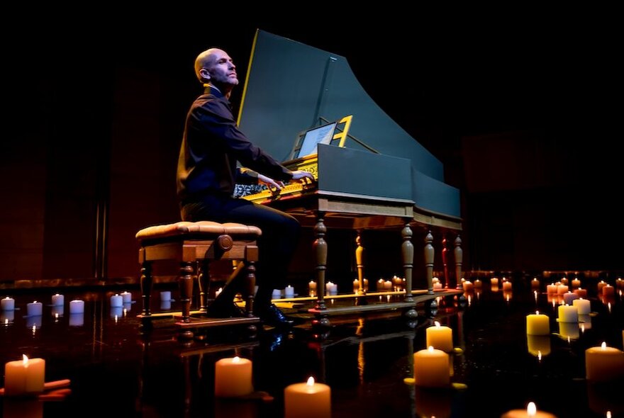 Classical musician, Erin Helyard, playing the harspichord on a darkened, candlelit stage.