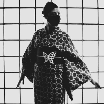 A black and white image of a woman wearing a kimono with a butterfly on the obi, and a face mask.