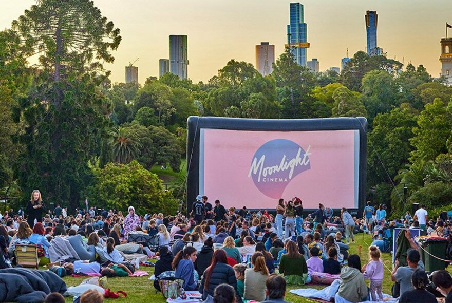 Crowd of people seated on the grass watching the Moonlight Cinema in the Royal Botanic Gardens.