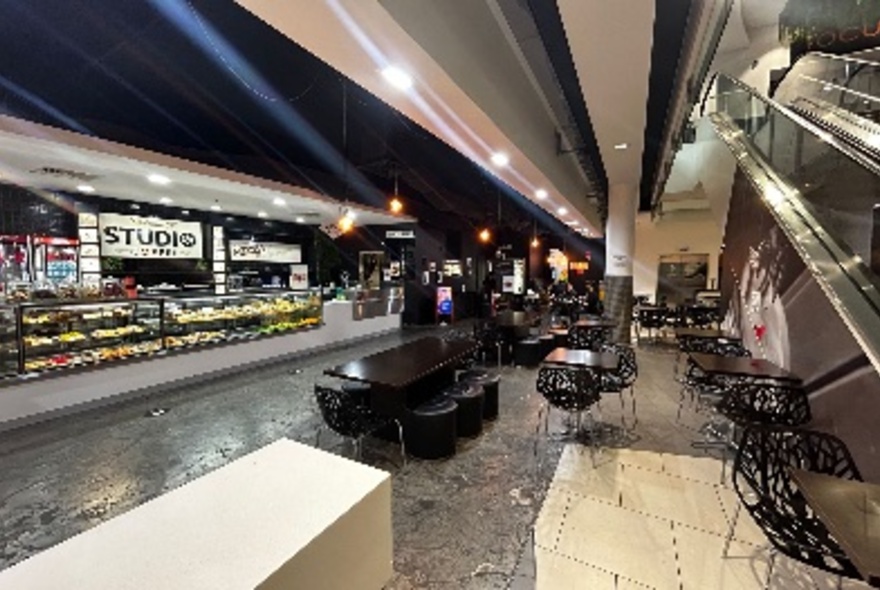 Studio Coffee food outlet with tables and chairs in front of the cafe, next to the escalator.