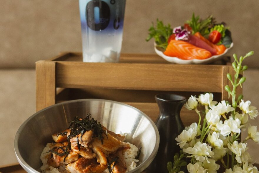 Bowls and plates of Japanese food on a table with flowers and pottery vase.