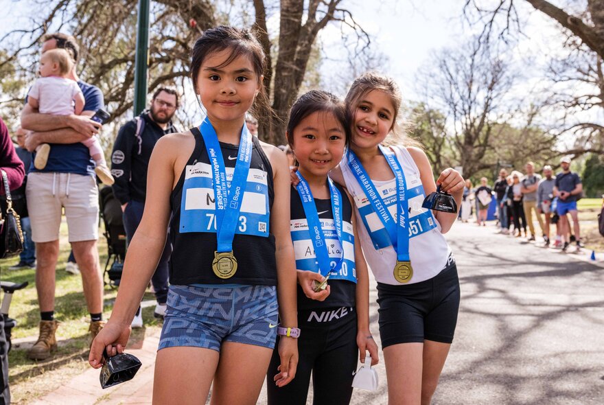 Three young athletes smiling together while wearing medals after a competitive running event outdoors.