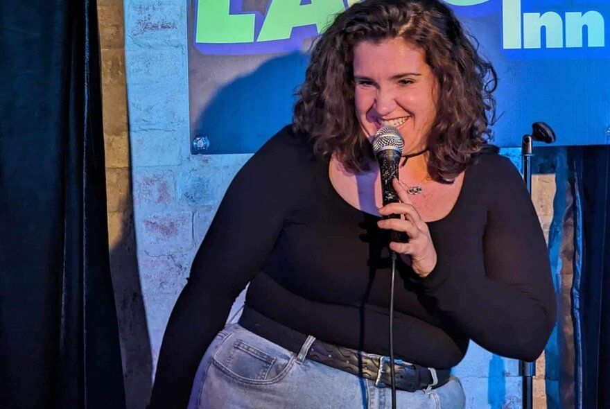 Woman performing with microphone on stage, smiling.