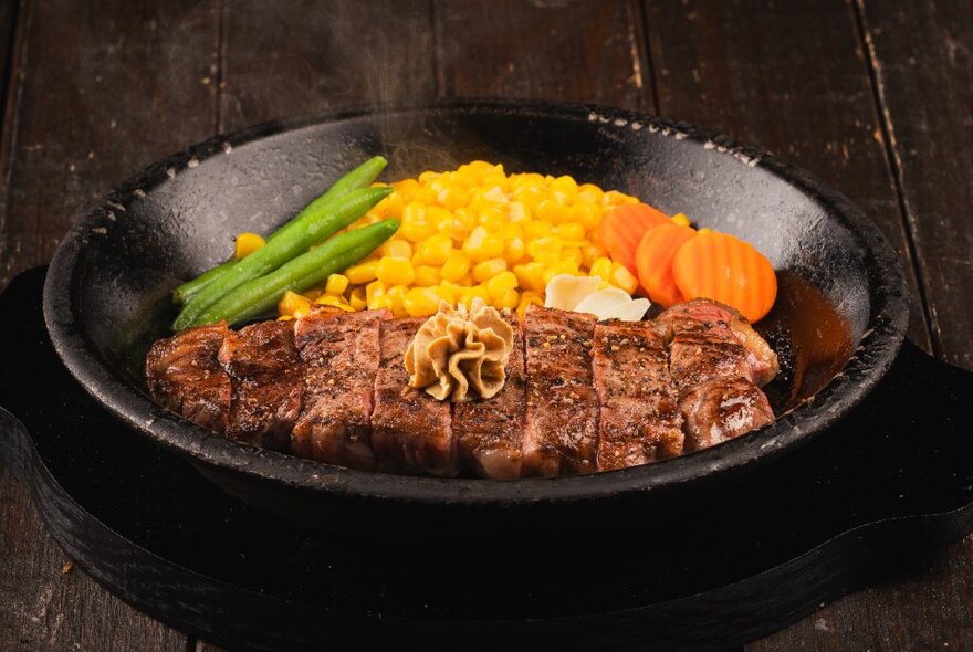 A dish of steak, beans, sweet corn and sliced carrots.