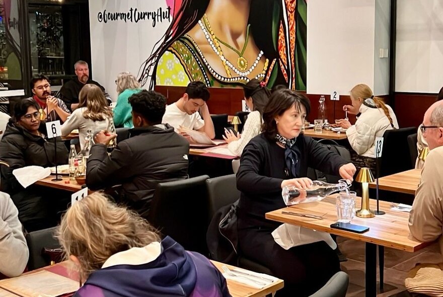 Patrons seated at tables at an Indian restaurant in various stages of ordering and eating.