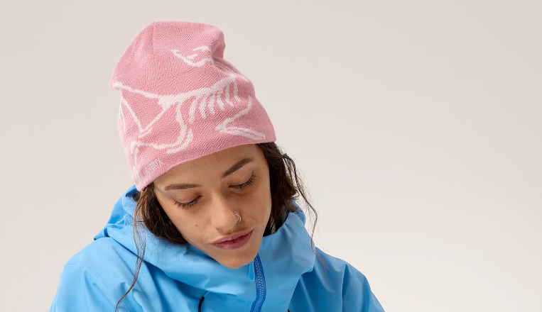 A model wearing a pink beanie with a white skeleton of a bird. 