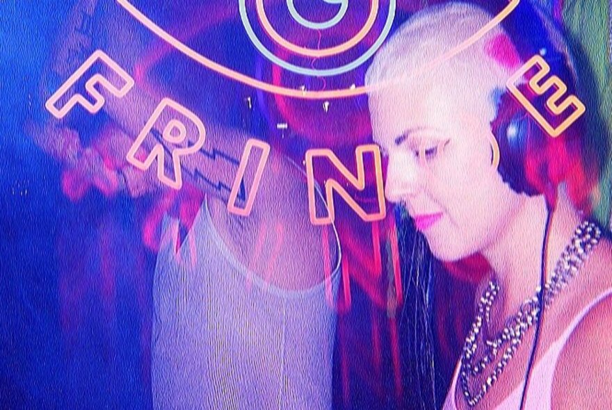A woman with a blonde buzzcut and headphones, and a man in a white singlet, partially obscured by neon lettering.