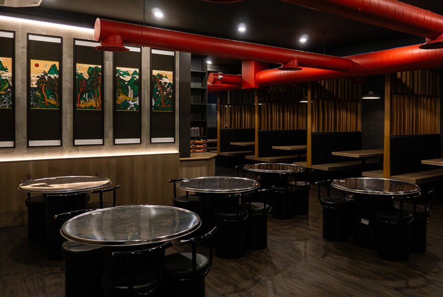 The interior of a restaurant with tables and chairs and downlights, a row of windows on the wall.