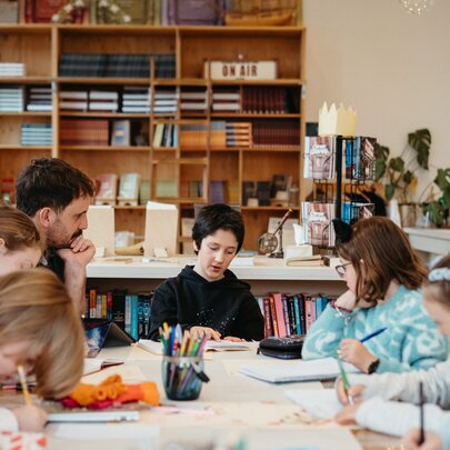 Young teens in a classroom setting with a teacher looking on and bookshelves in the background.