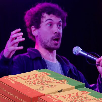 A man talking into a microphone he holds in his hand, with pizza boxes in the foreground.
