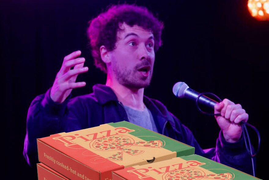 A man talking into a microphone he holds in his hand, with pizza boxes in the foreground.