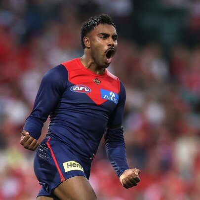 A Melbourne AFL player cheering himself and his team on the field with his mouth wide open, both his fists clenched and by his side as he runs. 