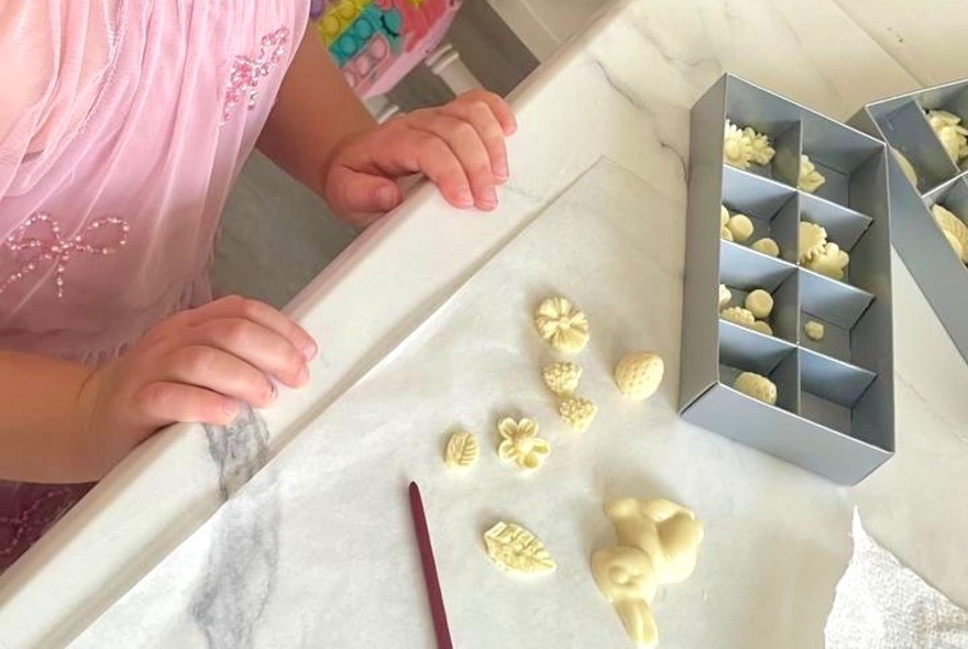Hands of a young child resting on a table, with white chocolate animal shapes in a box on the table.