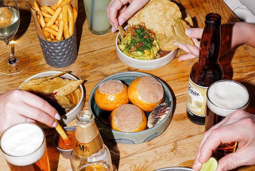 Looking at a table set with small plates of Mexican food, beers and chips.