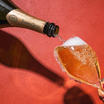 A bottle of champagne being poured into an overflowing champagne glass held on an angle by a woman's hand.