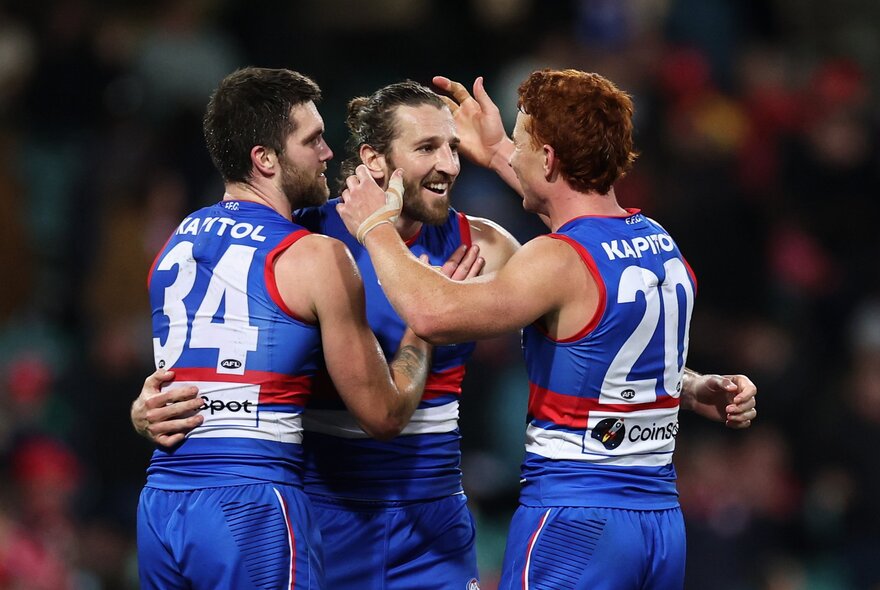 Three Western Bulldogs AFL players celebrating during a match.