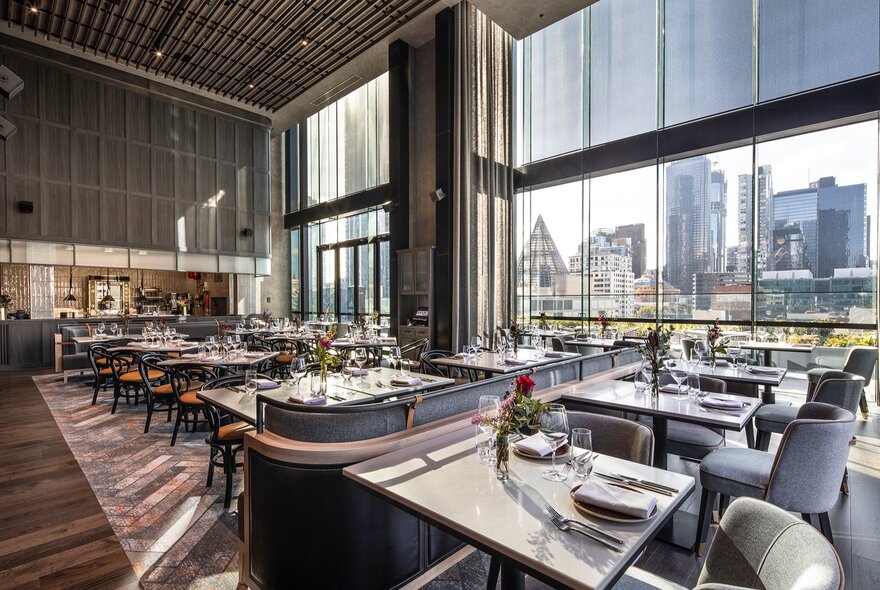 The interior of a restaurant with sky-high windows and a city view.