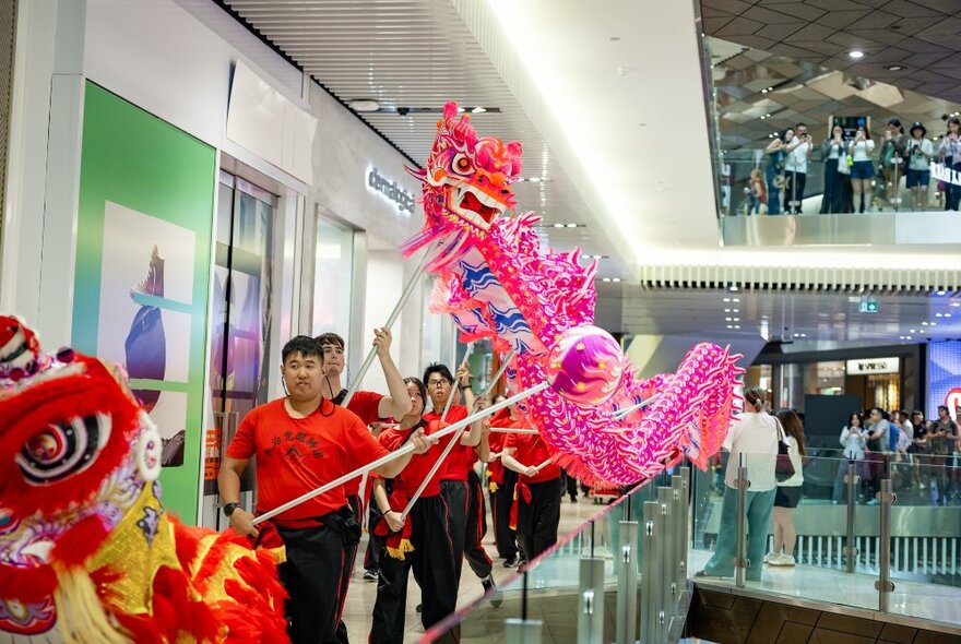 A lion dance taking place on an upper walkway Emporium Melbourne shopping centre, to celebrate the lunar new year, with shoppers observing the celebration. 