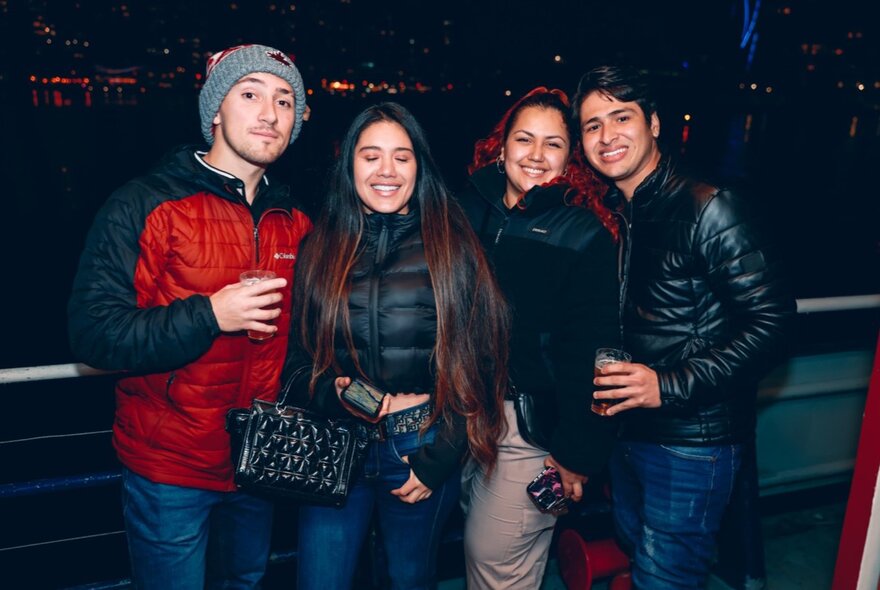 A group of four friends on the deck of a boat at night, smiling at the camera.