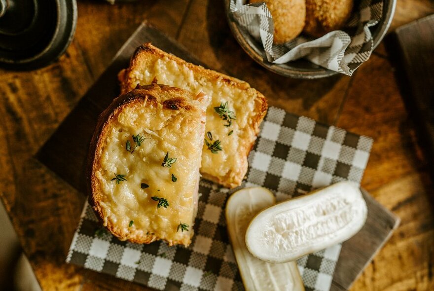 A croque monsieur cut in half on a plate with a giant sliced pickle.