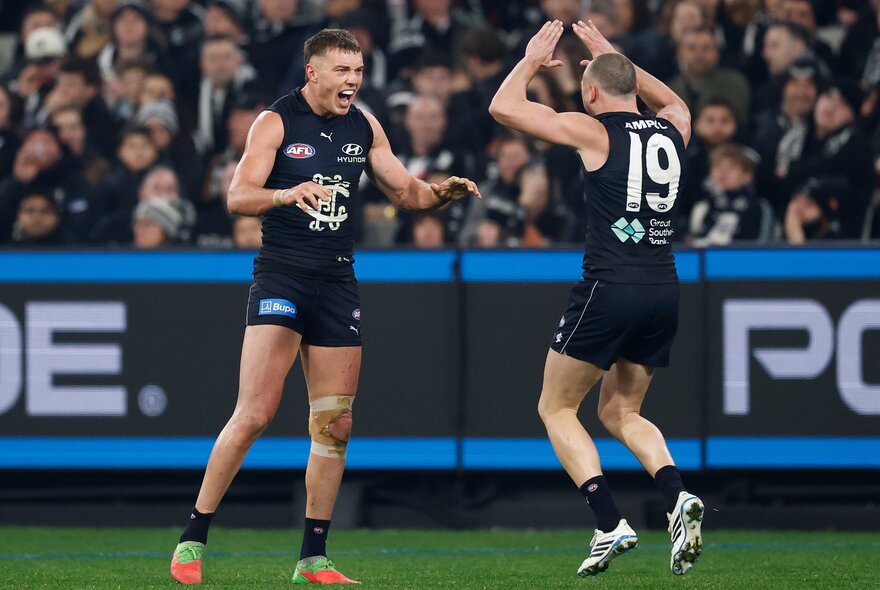 Two Carlton Blues AFL players about to give each other a double high five in celebration during a game.