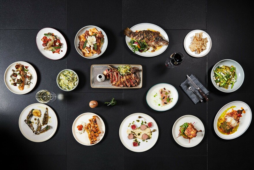 A selection of plates of food surrounding a central steak platter.