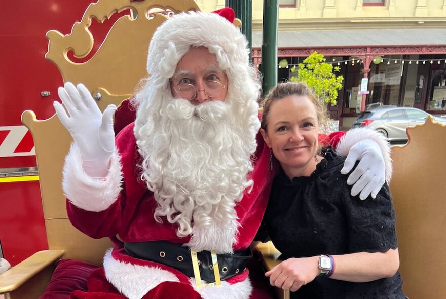 A young woman in a black top poses with Santa.