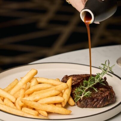 Gravy being poured onto a plate of steak and chips at a restaurant table.