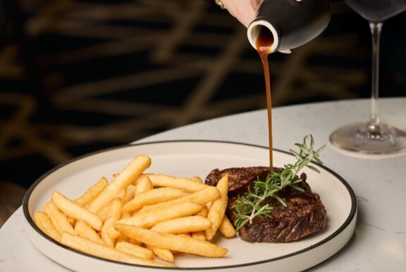 Gravy being poured onto a plate of steak and chips at a restaurant table.