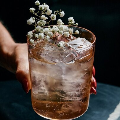 A hand holding a cocktail that has a flower in it.