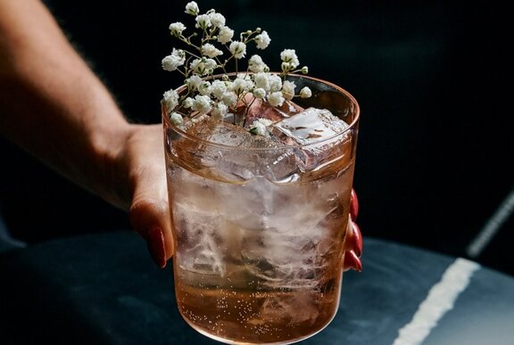 A hand holding a cocktail that has a flower in it.