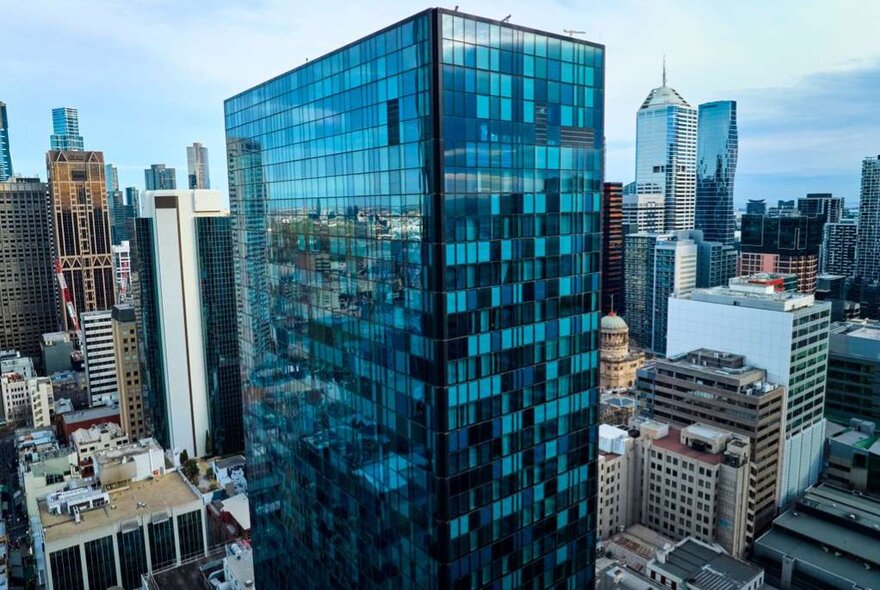 Glass skyscraper with blue windows in a city-centre locatio nsurrounded by midrise buildings.
