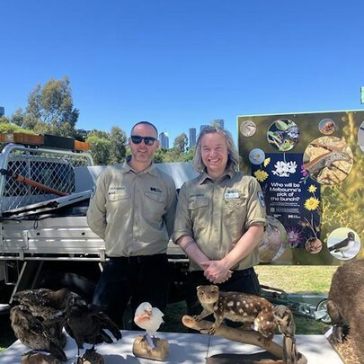 Two park rangers in front of a display table with their ute behind and more displays.